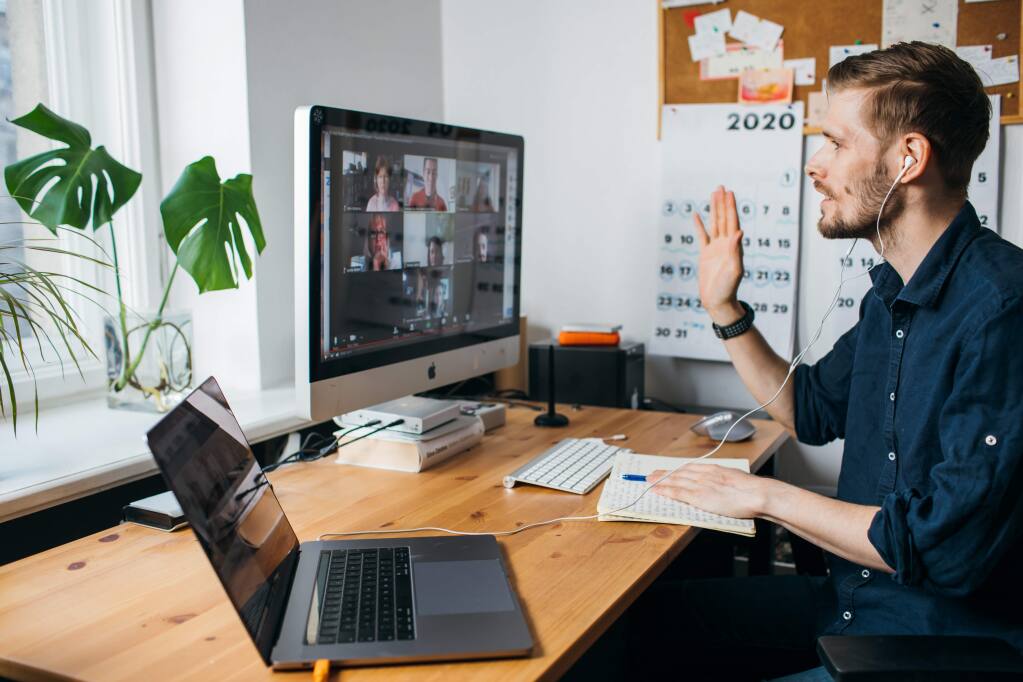 man at desk waving at Zoom call on computer monitor