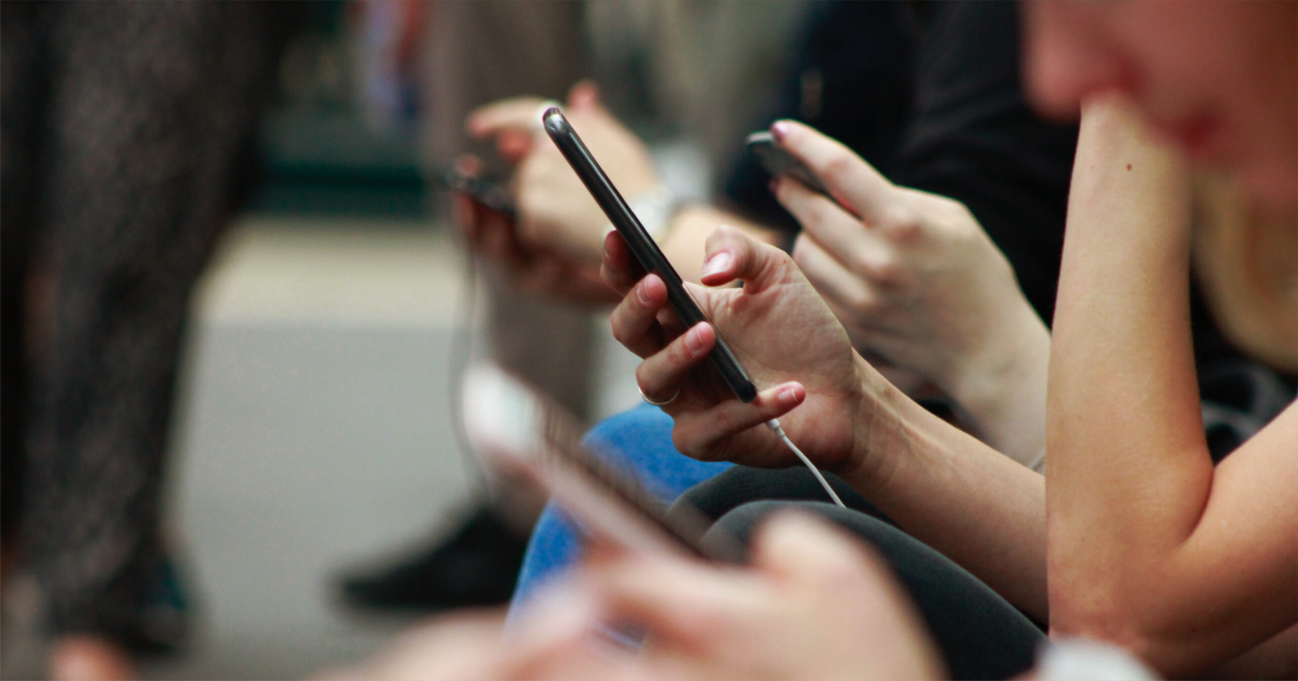 Close up of people sitting on a bench and scrolling on social media on their phones.