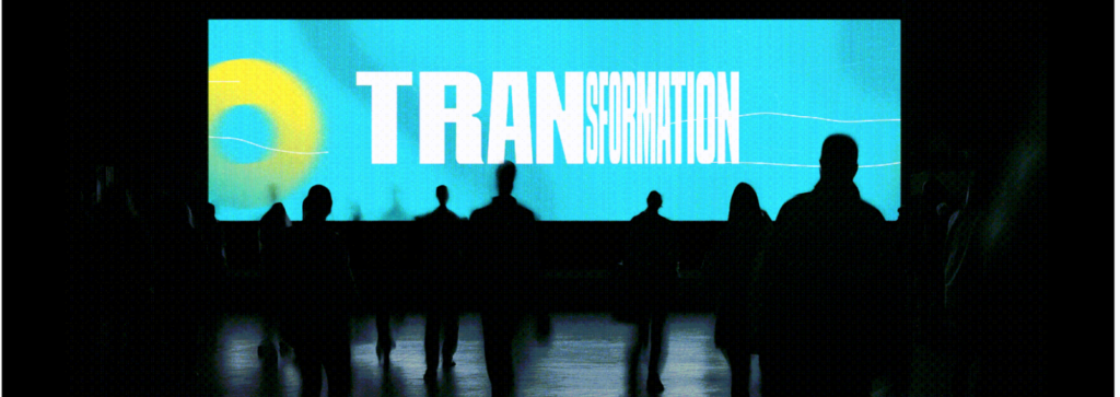 Silhouettes of people stand before a large screen displaying the word "TRANSFORMATION" on a blue background.