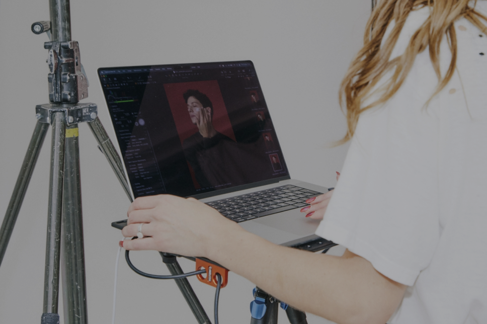 A person stands at a laptop showing a photo editing program with a portrait image on the screen, exemplifying how embedded creative teams like those at Microsoft collaborate, next to a tripod.