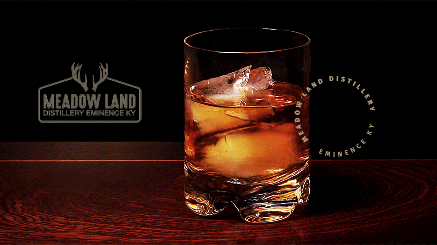 A glass of whiskey with ice sits on a dark wooden surface, highlighting the Meadow Lands brand, with "Meadow Land Distillery Eminence KY" logos in the background.