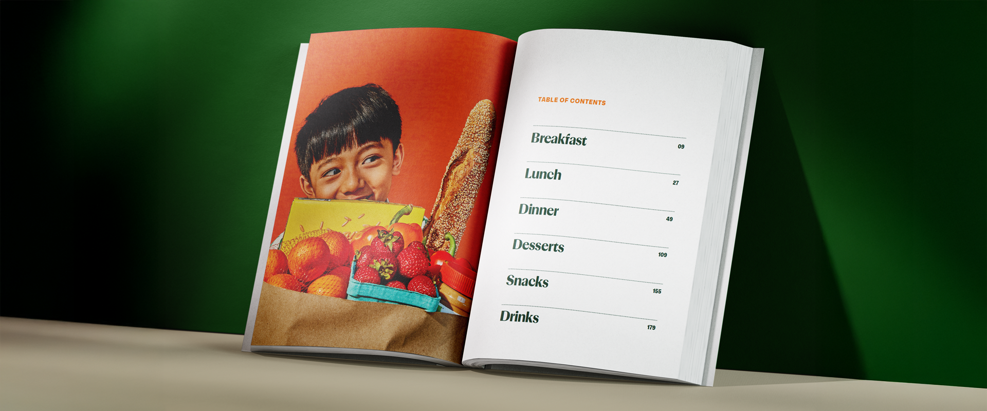 An open cookbook displays a photo of a smiling child holding a grocery bag on the left and a table of contents with meal categories on the right.
