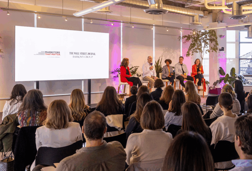 A panel of five speakers sits on stage in front of an audience, with a large screen displaying "Marketers That Matter" and "The Wall Street Journal" logos, highlighting the power of the marketers community in shaping the future of marketing.