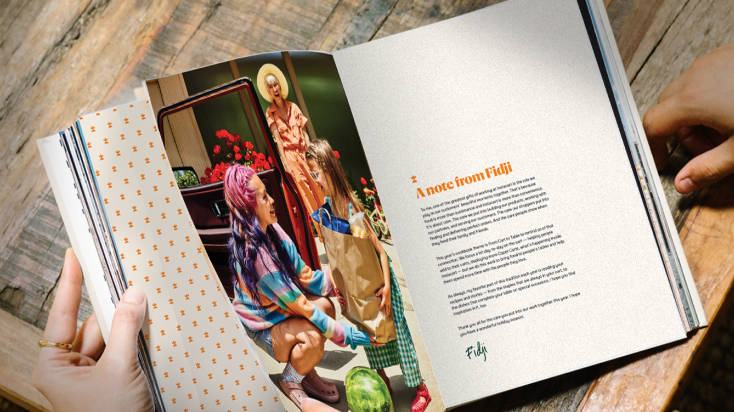 A person holds open a magazine showing a photo of people with groceries and a note titled “A note from Fidji” on the opposite page.