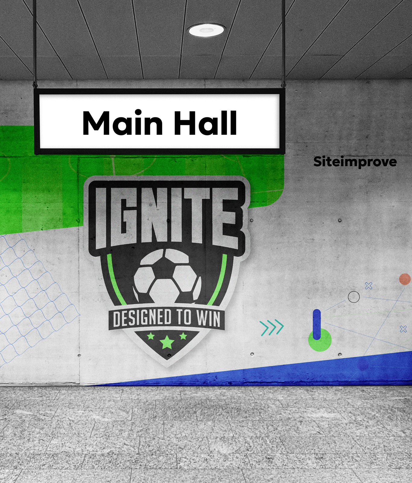 A sign reading "Main Hall" hangs from the ceiling; below is a wall mural with a soccer logo labeled "IGNITE Designed to Win," reflecting team spirit and featuring the word "Siteimprove" in the background.