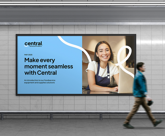 A digital billboard in a subway station displays an ad for Central, the Agency of Record for foodservice equipment and supplies solutions, featuring a smiling woman in an apron. A person walks by.