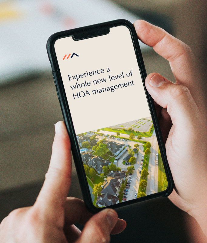 Person holding a smartphone displaying "Experience a whole new level of HOA management" above an aerial view of a residential neighborhood, showcasing RealManage’s innovative property management SaaS and strong brand identity.