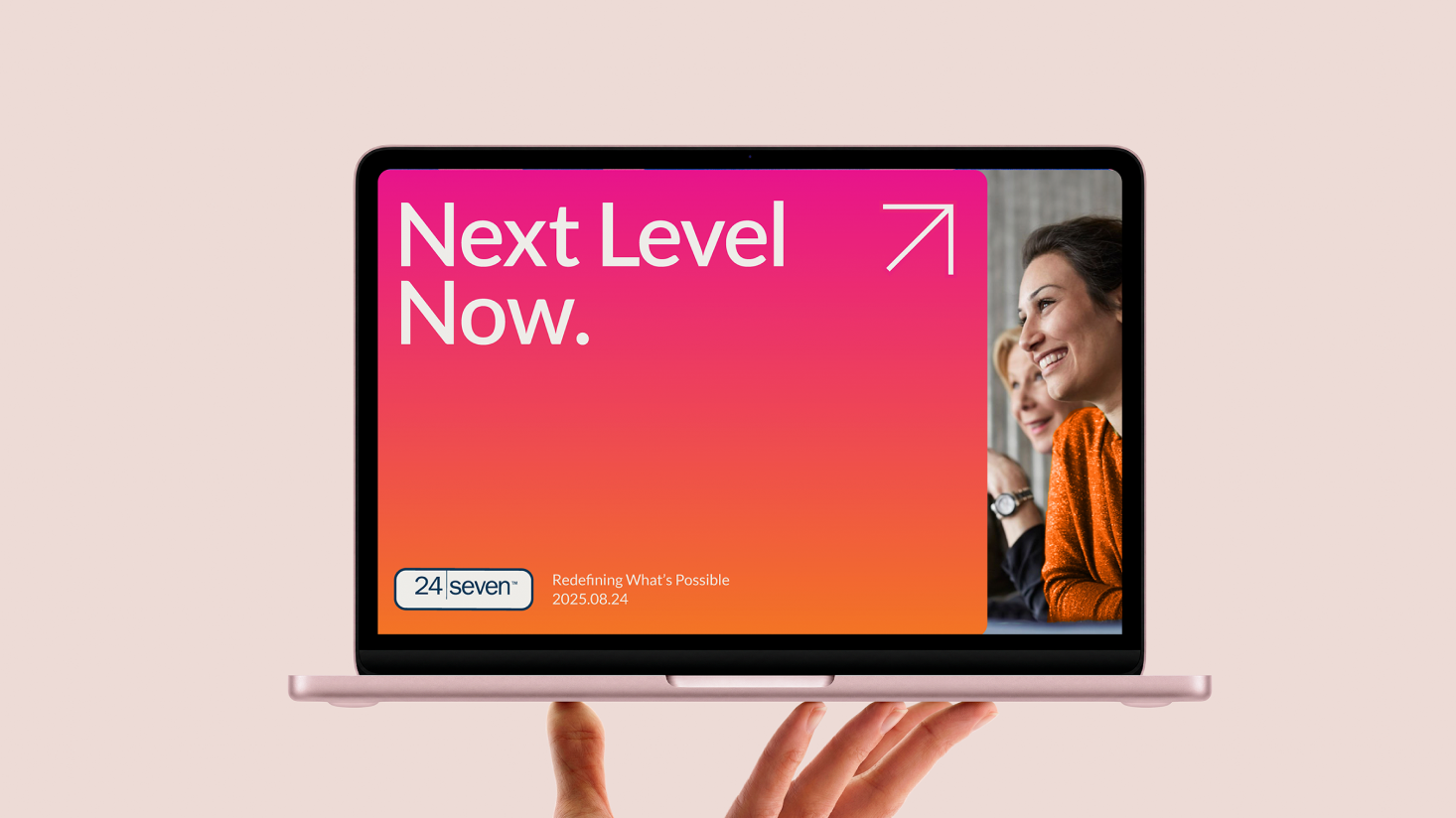 A hand holds a laptop displaying a slide with "Next Level Now," celebrating 25 years of 24 Seven and next-level success, featuring smiling people, a logo, date, and an upward arrow.
