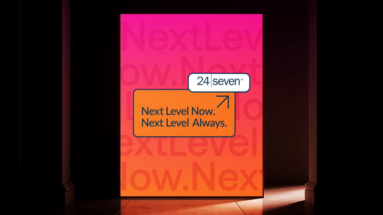 A backlit display reads “24 Seven. Next Level Now. Next Level Always.” with a gradient pink and orange background featuring the words “Next Level” in large faded text, celebrating 25 years of next-level success.