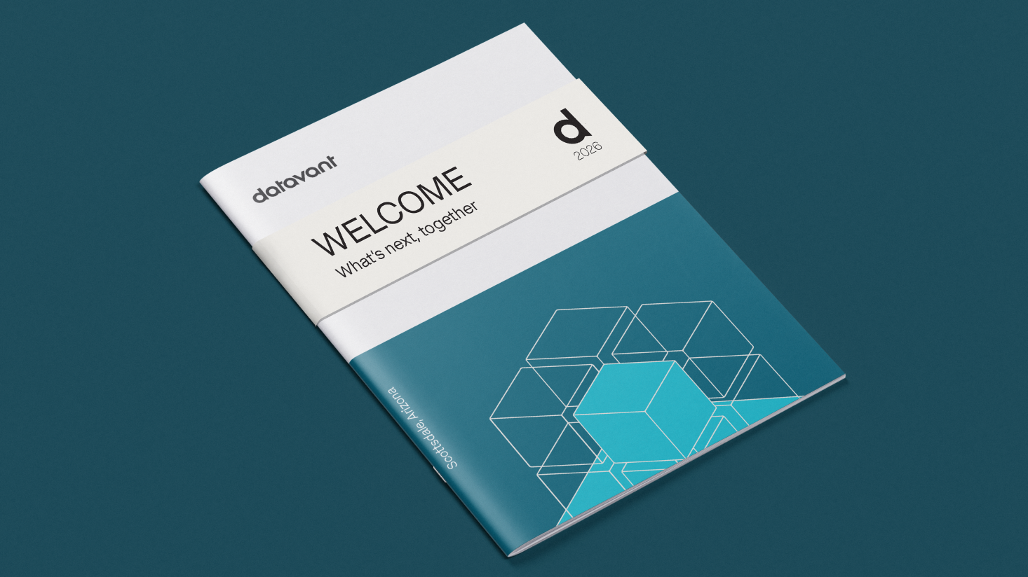 A booklet with the Datavant logo, "WELCOME: What's next, together," "d 2023," and a geometric hexagon pattern on the cover, placed on a dark teal surface—perfect for a premium executive experience.