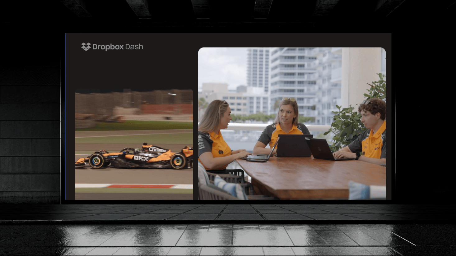 A McLaren race car on a track is shown beside three people in matching uniforms sitting at a table outside, working on laptops and talking, possibly collaborating with AI tools like Dropbox Dash to analyze performance data.